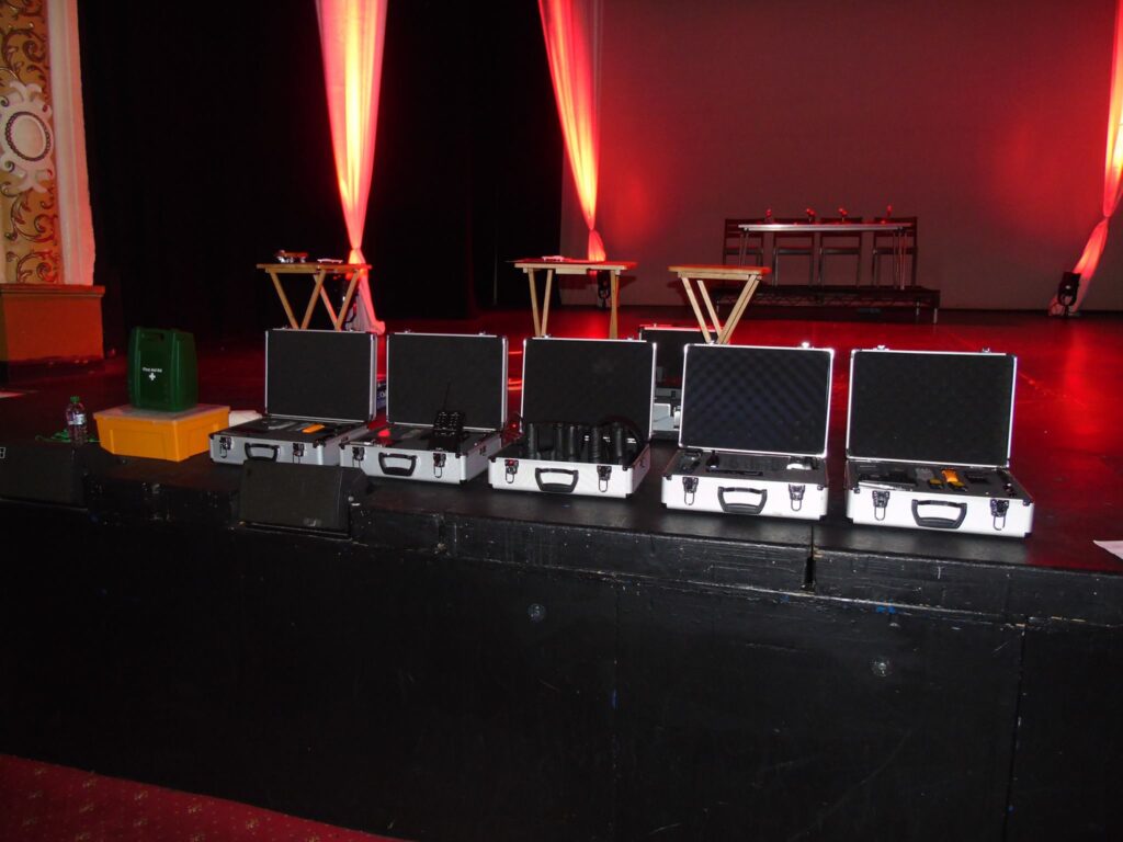 Blog 38 Ghost Hunting Equipment and Experiences. Ghost hunting equipment arranged on a dimly lit theatre stage, including EMF meter, digital voice recorder, flashlight, and camera. Ghost Hunting Equipment and Experiences: Your Essentials!